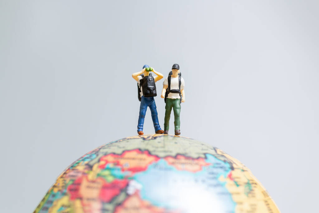 Travelers in miniature, standing on the globe and making their w Travelers in miniature, standing on the globe and making their way to their destination, Travel concept